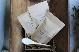 three brown tea pouches in a wooden box with a spoon