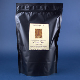 shiny black tea pouch bag with orange rectangle on label against a blue backdrop