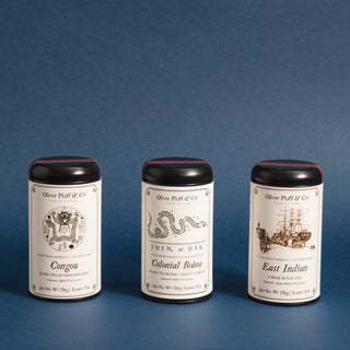 three black tea tins with black and white graphics of sailing ship, a snake and and flowery design against a blue background