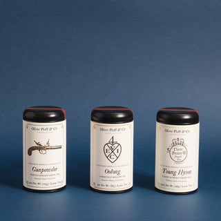 three black tea tins in a row with differing labels. A heart, gun, and circle. blue background