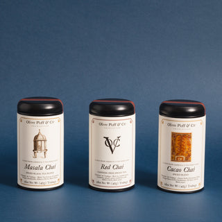 three black tea tins in a row with different colored graphics on each label in front of blue backdrop