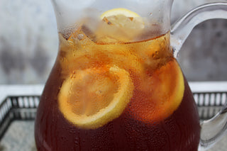 glass pitcher of iced tea with lemon slices on silver platter