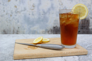 iced glass of tea with lemon slice on it with a cutting board and knife