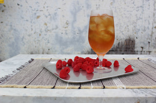 glass of iced tea with red raspberries sprinkled beside it on a silver platter