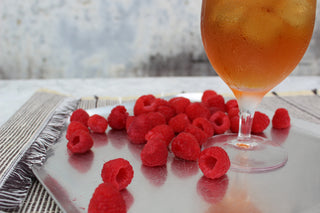 glass of iced tea with red raspberries sprinkled beside it on a silver platter