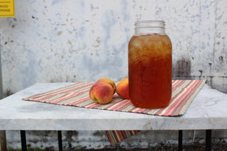 large glass mason jar filled with iced peach tea, sitting beside 3 peaches outside