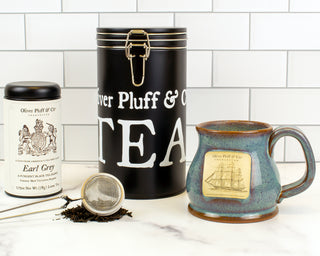 black latch tin, ceramic mug, mesh tea strainer and Earl Grey tea sitting on counter