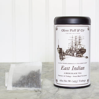 black tea tin with old timey ship and a white mesh tea bag beside it on white kitchen counter