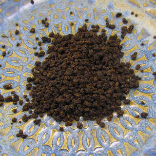 pile of dark loose leaf tea on blue and yellow plate