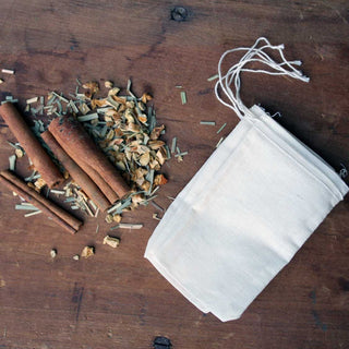 brown cinnamon sticks and loose leaf tea leaves laying beside white tea mesh tea bags on wooden table