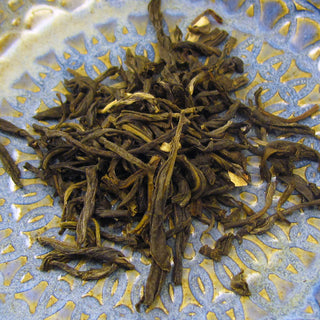 zoomed in view of long golden loose leaf tea piled on yellow and blue plate