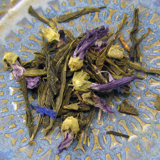 pile of purple flower pedals and golden loose leaf tea on blue and white plate