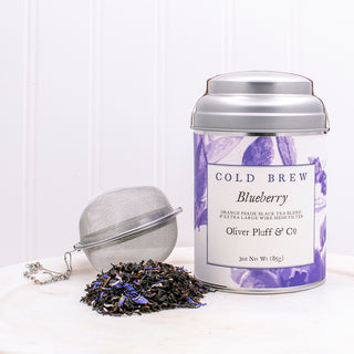 silver tea tin with blueberry graphics, loose leaf tea and a mesh tea holder placed on white kitchen counter