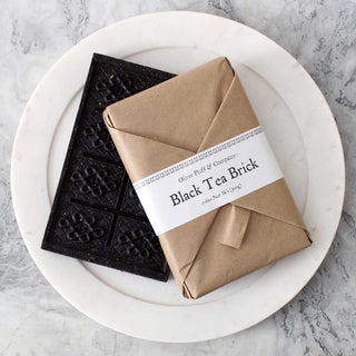 black tea brick with another wrapped tea brick in brown paper on white plate