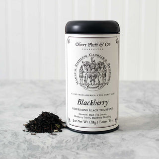 black tea tin with pile of loose leaf tea beside it standing on white counter