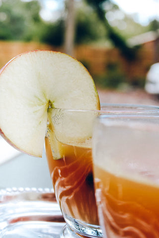 fresh apple slice hanging on side of clear cold tea glass