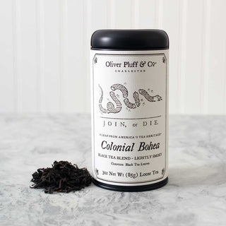 black tea tin with snake graphic on label and a small pile of loose leaf tea beside. Sitting on white kitchen counter