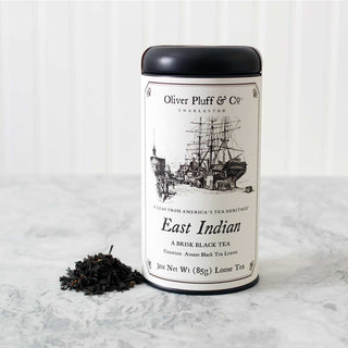 black tea tin with old timey ship on label beside a pile of loose leaf tea sitting on white counter