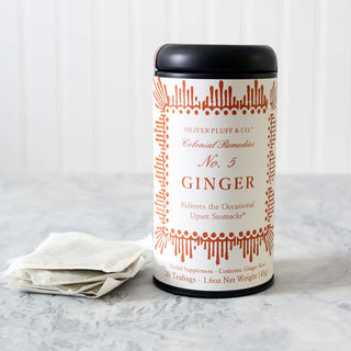 black tea tin with orange pattern against sitting beside stack of white mesh tea bags on marble kitchen counter