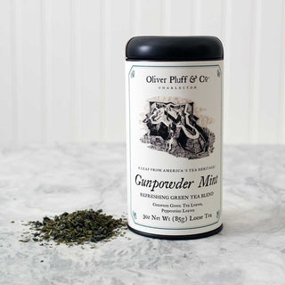 black tea tin with old timey graphic on label with pile of loose leaf tea beside it on white kitchen counter