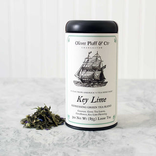 black tea tin with old timey ship on label sitting beside pile of loose leaf green tea