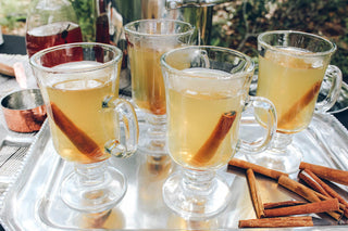 4 clear drinking classes filled with tea and a cinnamon stick in each one, sitting on silver platter outside